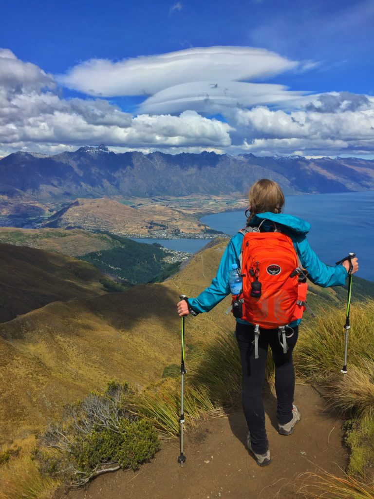 A KUHL Ambassador reaching a mountain peak with KUHL women's hiking clothing and trekking poles