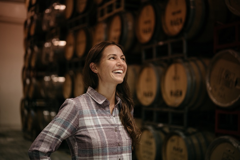 Wine and Adrenaline - a woman smiling in a wine basement dressed in KUHL clothing