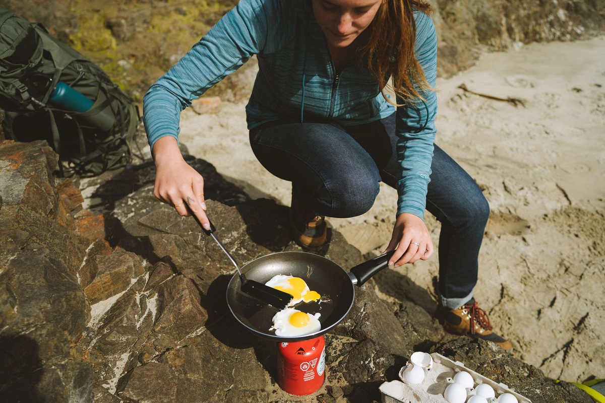 woman frying eggs outdoors in a pan