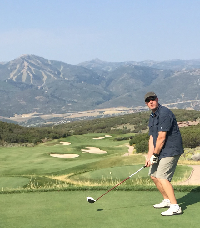 KUHL Sponsored Golf Course Hole - A man dressed in KUHL Golf Shorts taking a swing with a mountainside in the back.