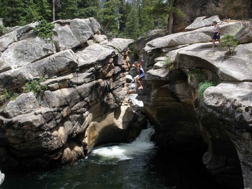 people jumping from a cliff into the water surrounded by rock formations