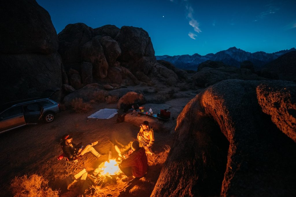 four people around the campfire next to car during night