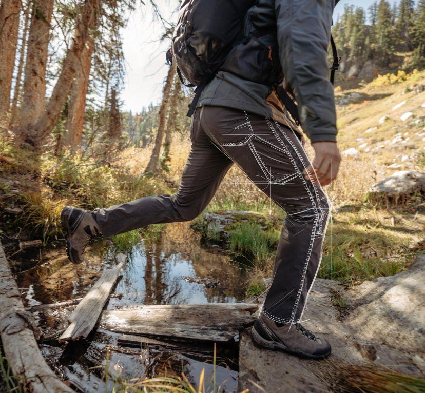 A man crossing a stream wearing his Kühl Radikl® pants.