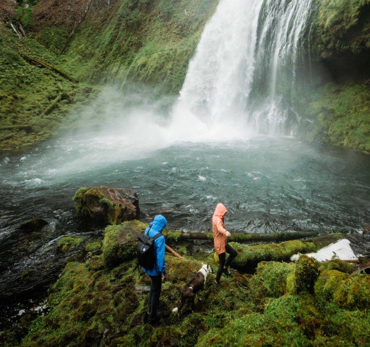 Two people visiting a waterfall wearing The One™ Shell jackets.