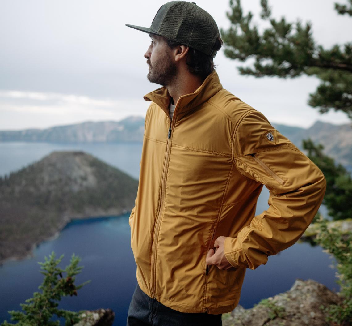 A man looking at the lake wearing his The One™ Jacket and his Flatbill Trucker cap.