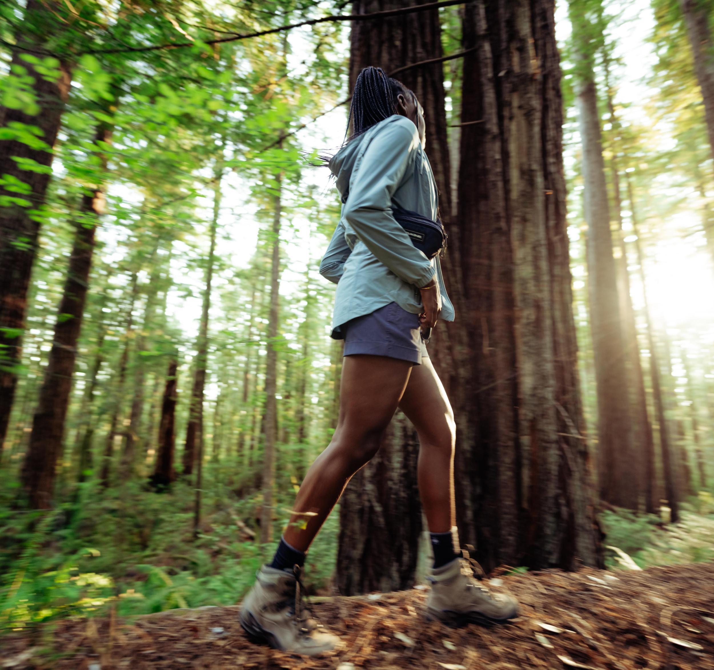 A woman walking through the woods wearing a pair of Kühl Haven™ Shorts.