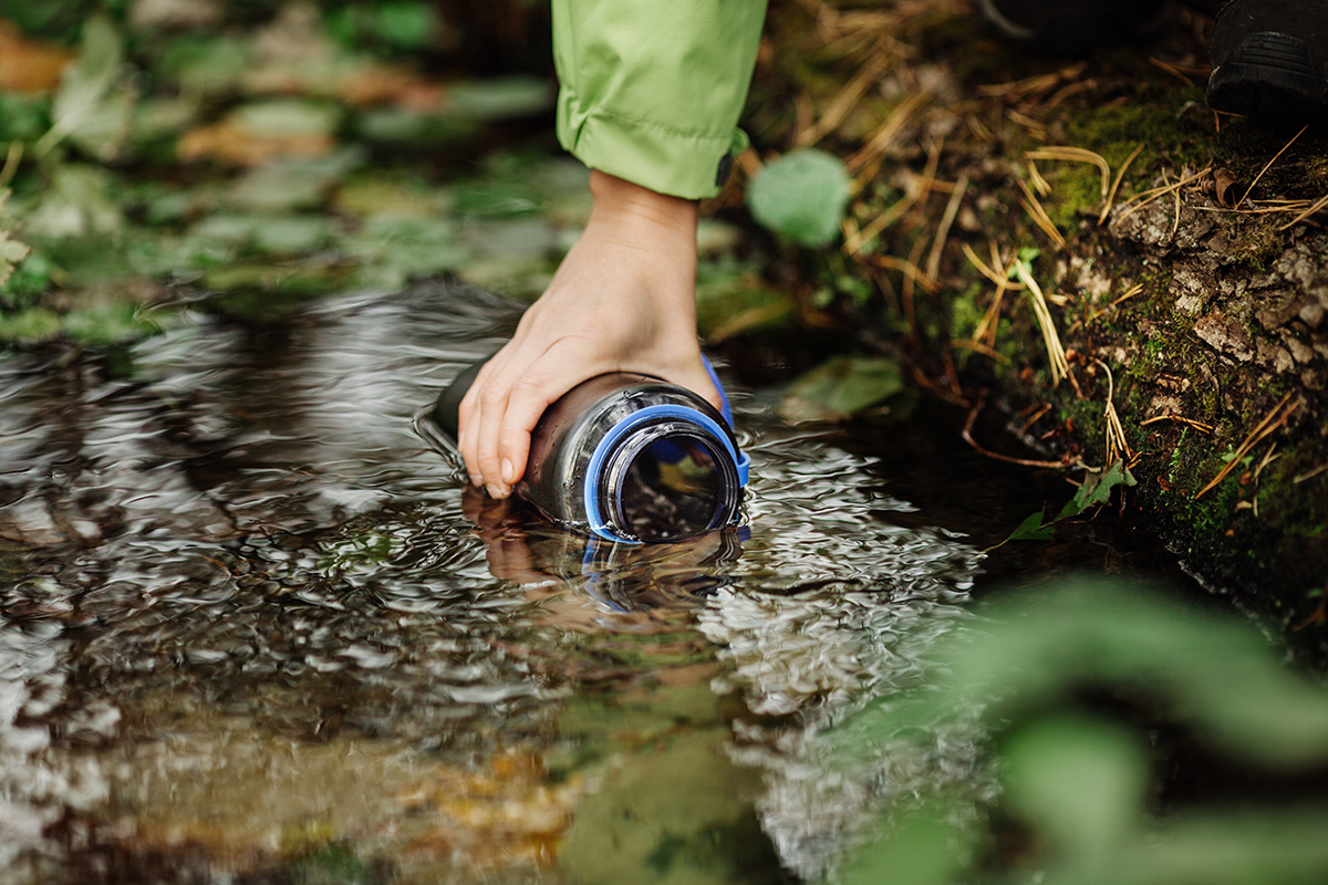 woman taking water from forest spring on hiking trip