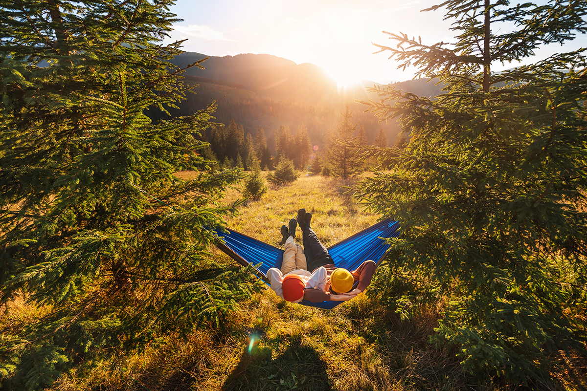 Children lie in tourist hammock in the forest on mountain landscape background. Top view, wide angle shooting.