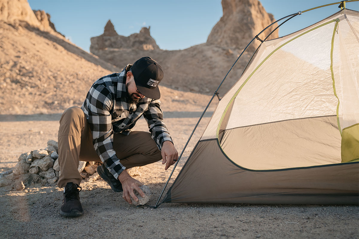 A man setting up a tent in a rocky mountain.