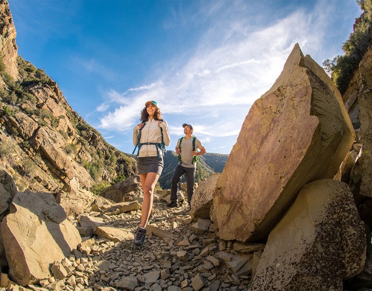 KUHL summer hiking clothing for men and women show by a man and a woman hiking on a rocky trail