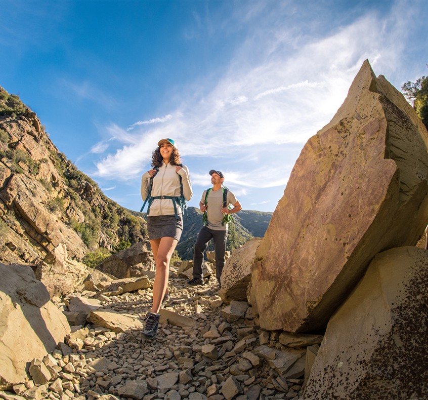 KUHL summer hiking clothing for men and women show by a man and a woman hiking on a rocky trail