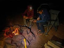 Two men sitting and reading next to a campfire during an evening. 