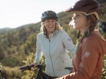Cina and Kate cycling in the backcountry dressed in women's outdoor clothing and hats.