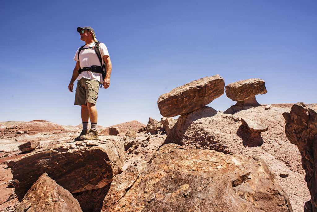 A man standing on a rock wearing KUHL men's climbing shorts, shirts, and hats
