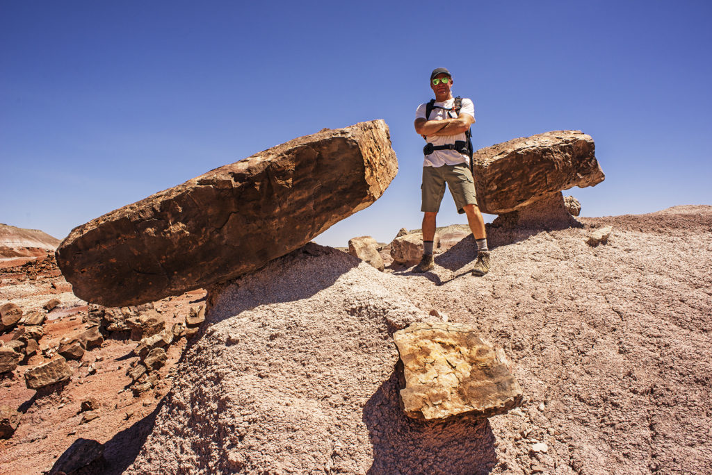 A man standing next to a rock wearing KUHL men's climbing shorts, shirts, and hats