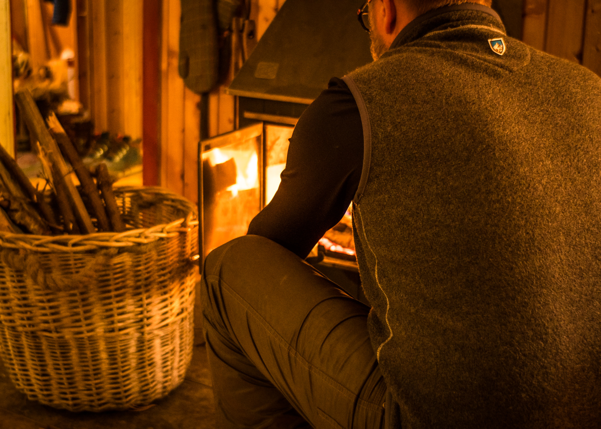 A man starting a fire in the hearth, dressed in KUHL mens fleece
