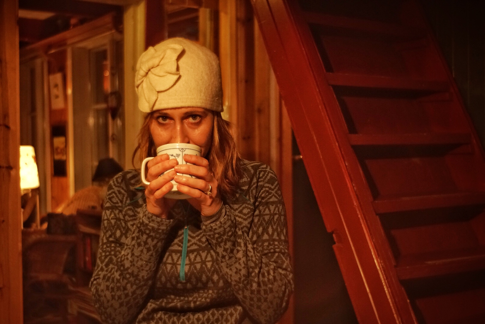 A woman starting in a cabin with KUHL women's fleece, drinking a warm drink