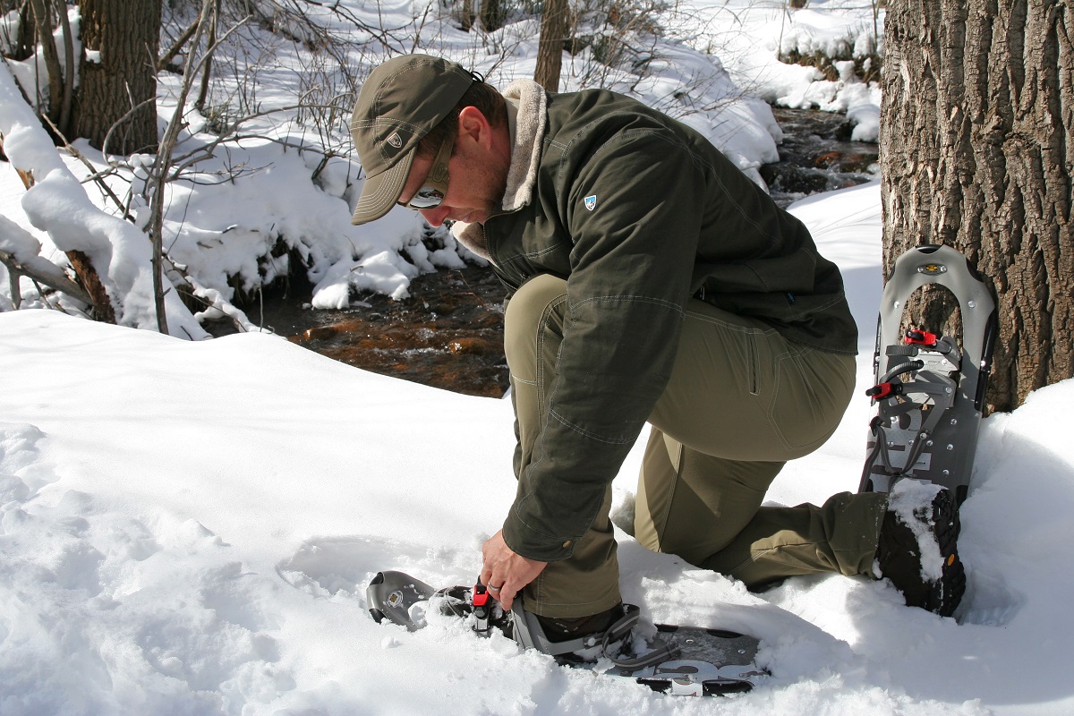 A man putting on a snowshoe on a snowy trail.