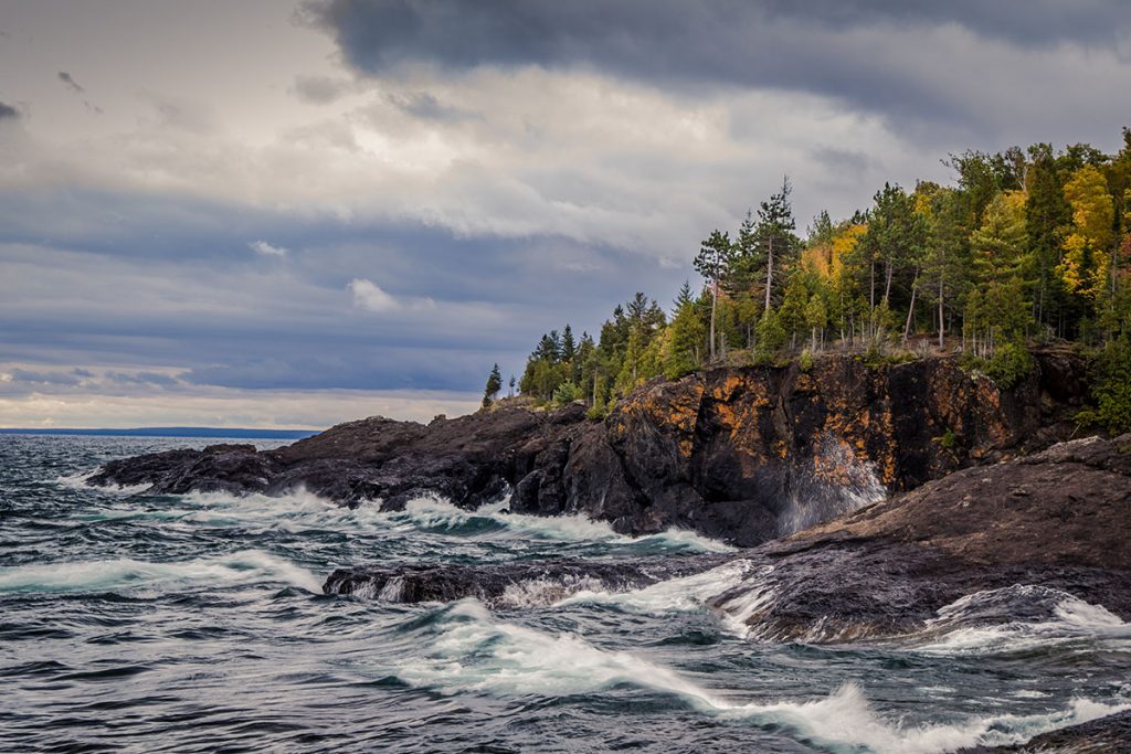 Gray sky and stormy seas crash on the cliffs of the black rocks along the shores of the Lake Superior coast