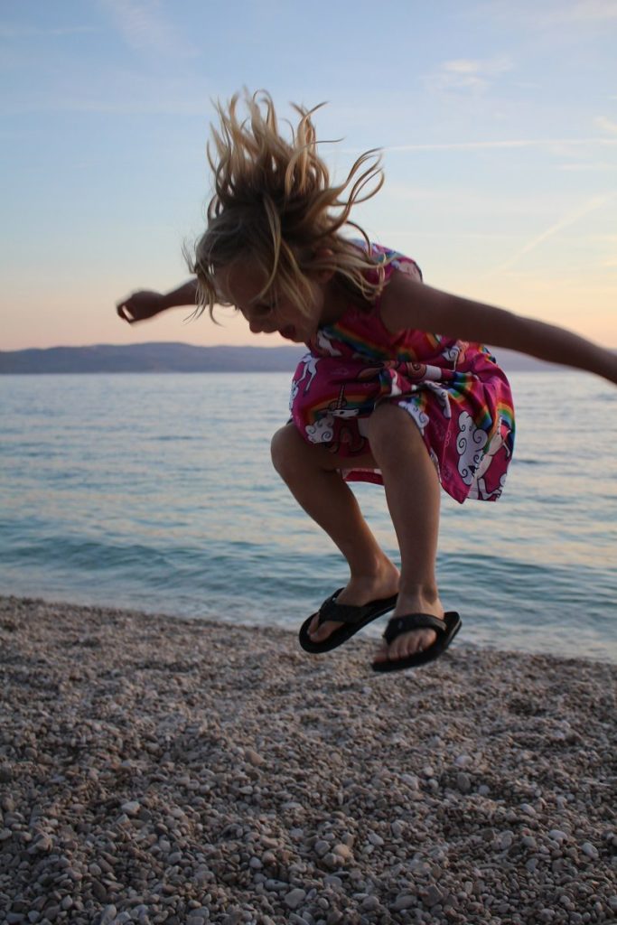 Blonde girl jumping on a pebble beach in Croatia.