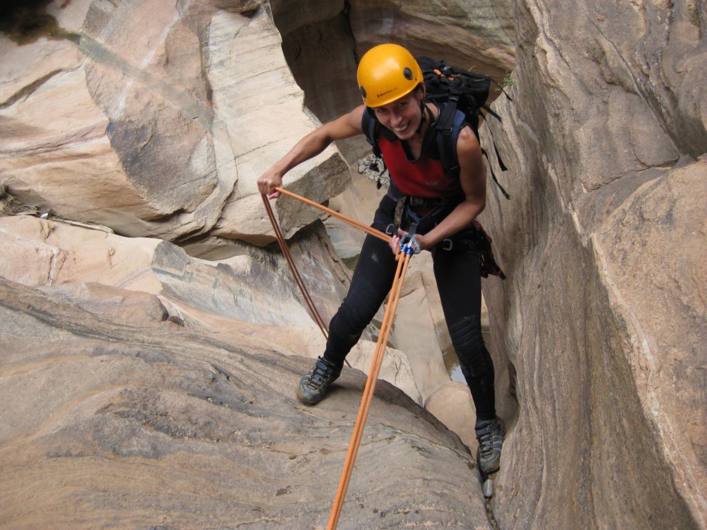 A woman in yellow helm climbing, smiling, and enjoying national parks such as Zion.