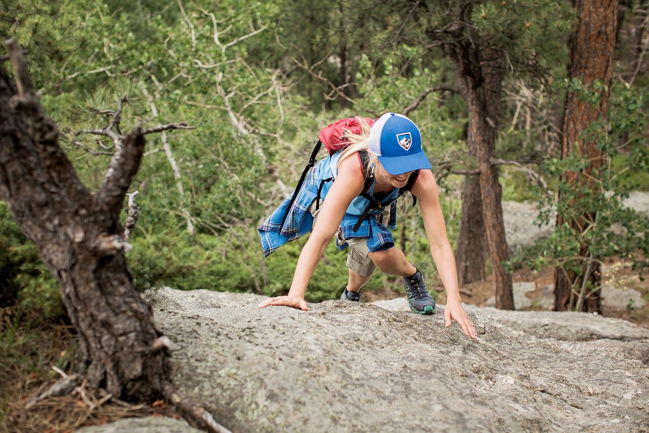 A woman wearing KUHL hat and gear climbs over a rock in the forest while on one of the hiking trails near Washington, DC.