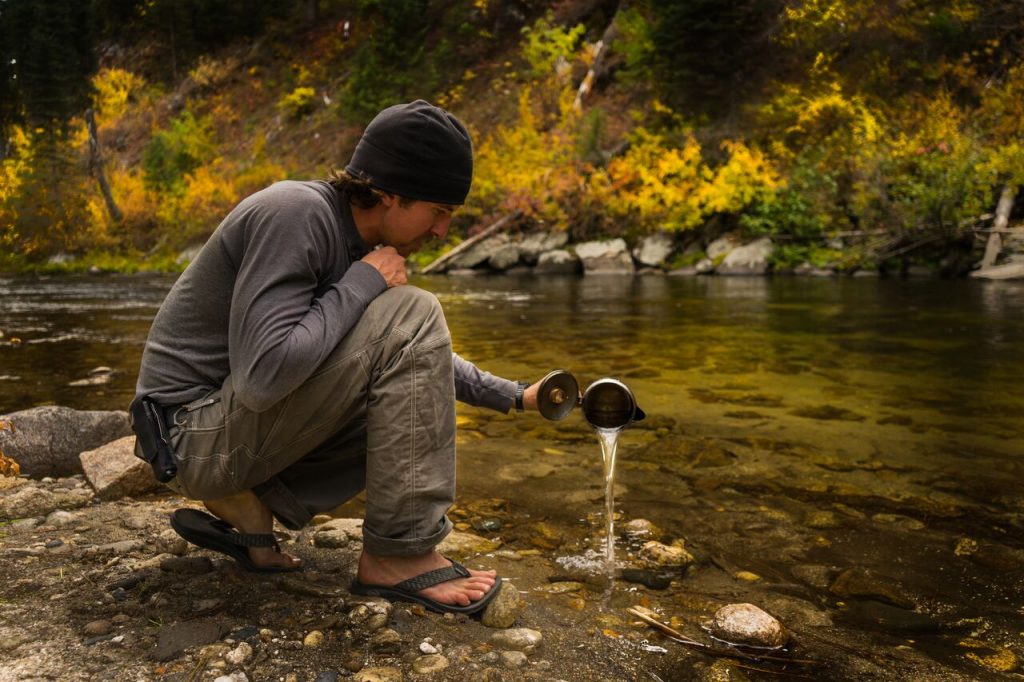 A man wearing KUHL Clothing men's hiking pants and men's long sleeve shirt pouring water in a creek.