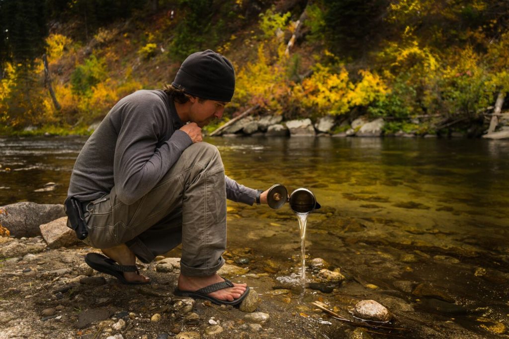 Guideposts for Planning Your Thru-Hike 3 A man wearing KUHL Clothing men's hiking pants and men's long sleeve shirt pouring water in a creek.