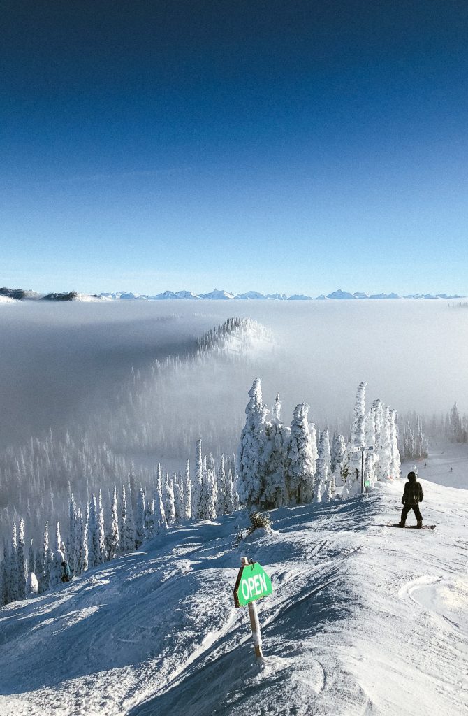 An open skiing slope with snow covered trees and fog in the distance during daytime.
