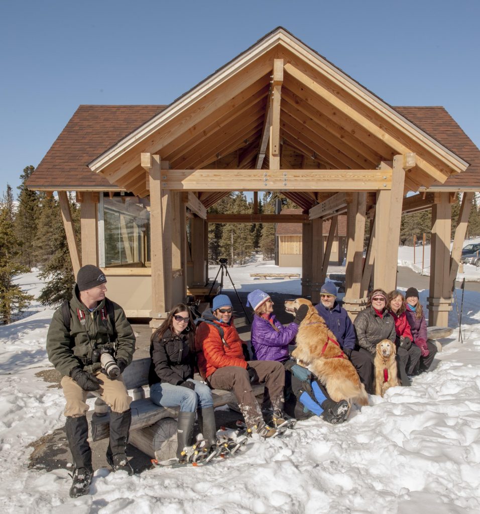 A group of skijoring enthusiasts resting next to a wooden cabin in the snow.
