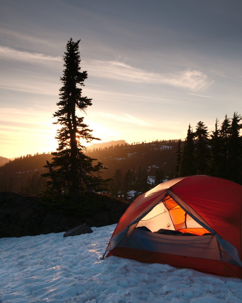 An orange dome tent near trees during sunrise