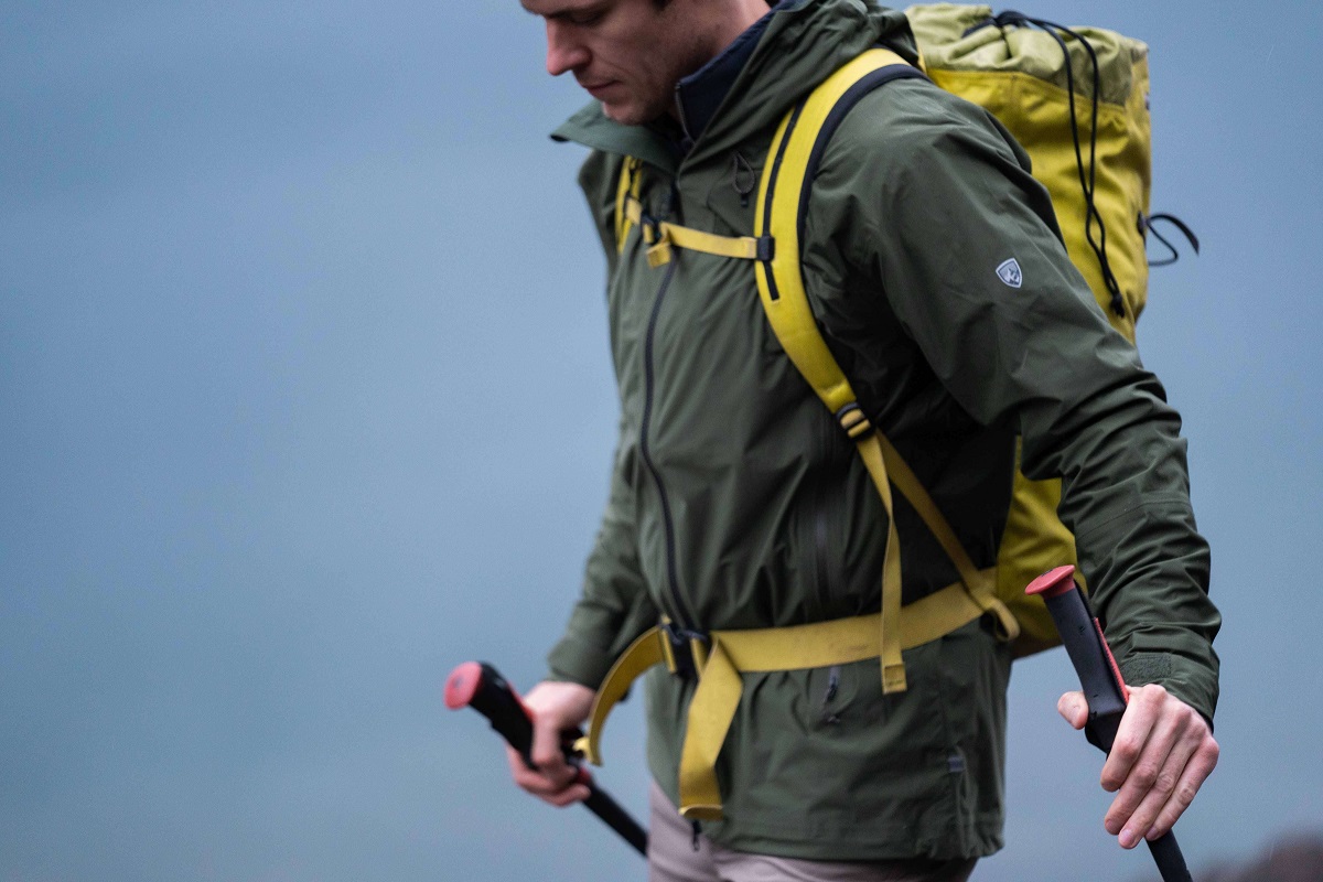 a man with shell jacket, yellow backpack and trekking poles