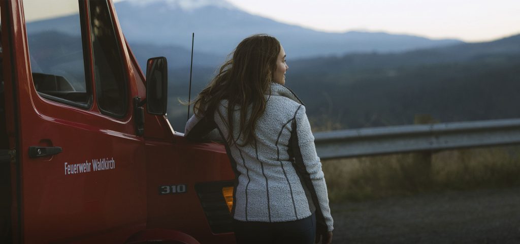 A woman leaning on a red truck wearing KUHL women's merino wool clothing