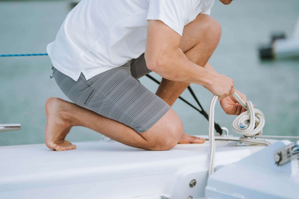 man kneeling on a boat holding rope knot