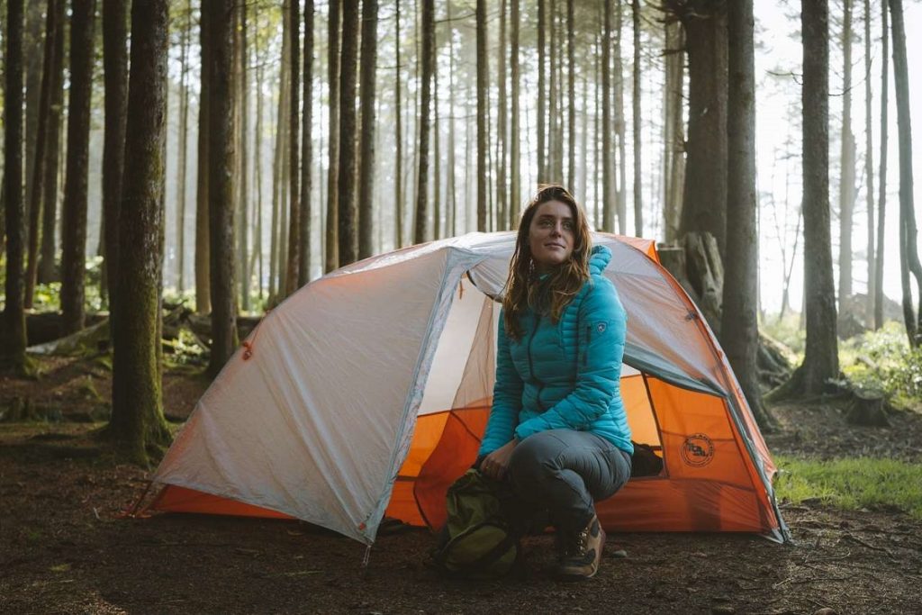 woman in blue jacket in front of orange tent in the woods