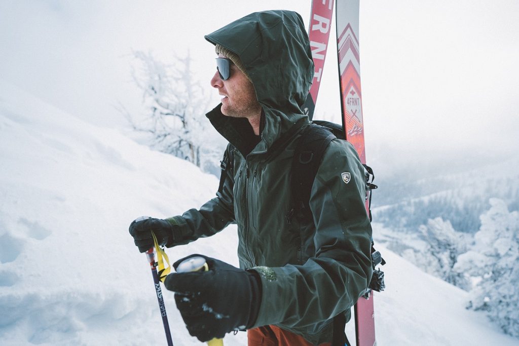 man with sunglasses on snowy ground holding ski poles
