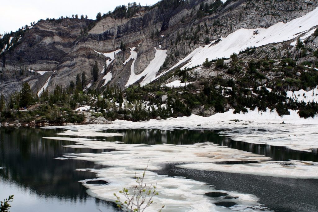 snow on body of water with snowy rock formations in the background
