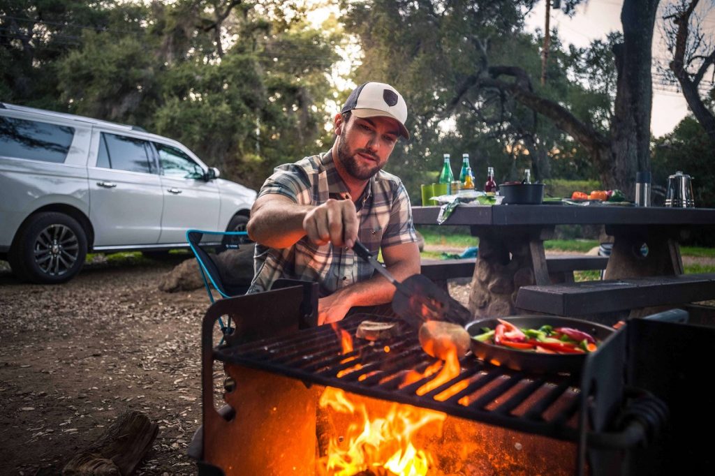 man in white hat and plaid shirt making food on camping grill