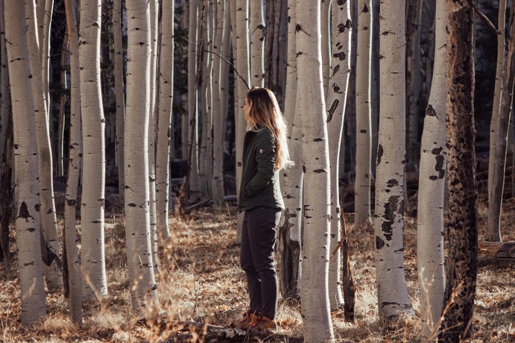 woman in KÜHL jacket standing between white trees