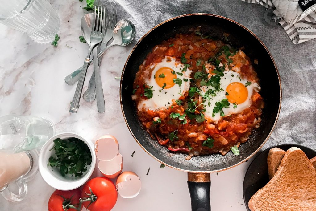 shakshuka eggs on black cooking pan next to fork and bread