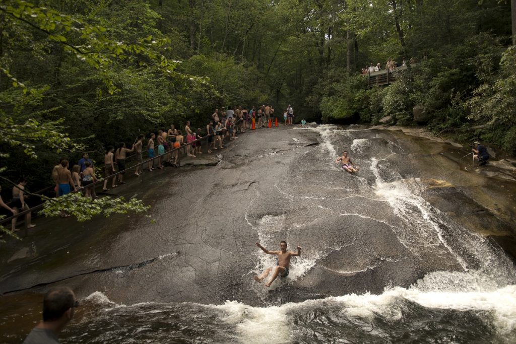 people sliding down the grey rock covered with water