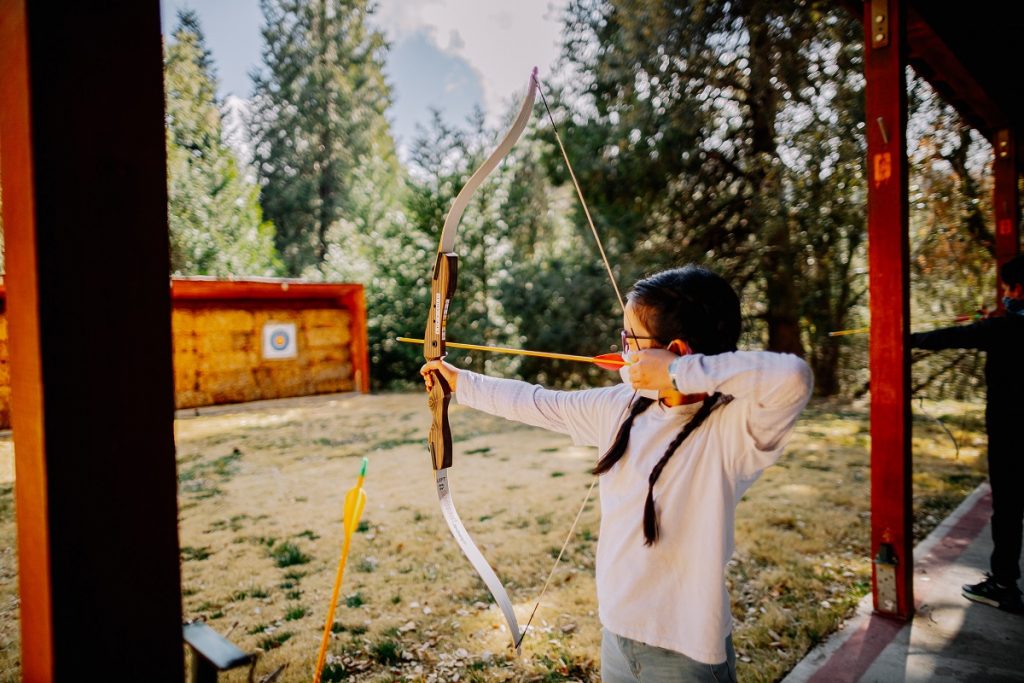 girl in white shirt holding brown bow and arrow