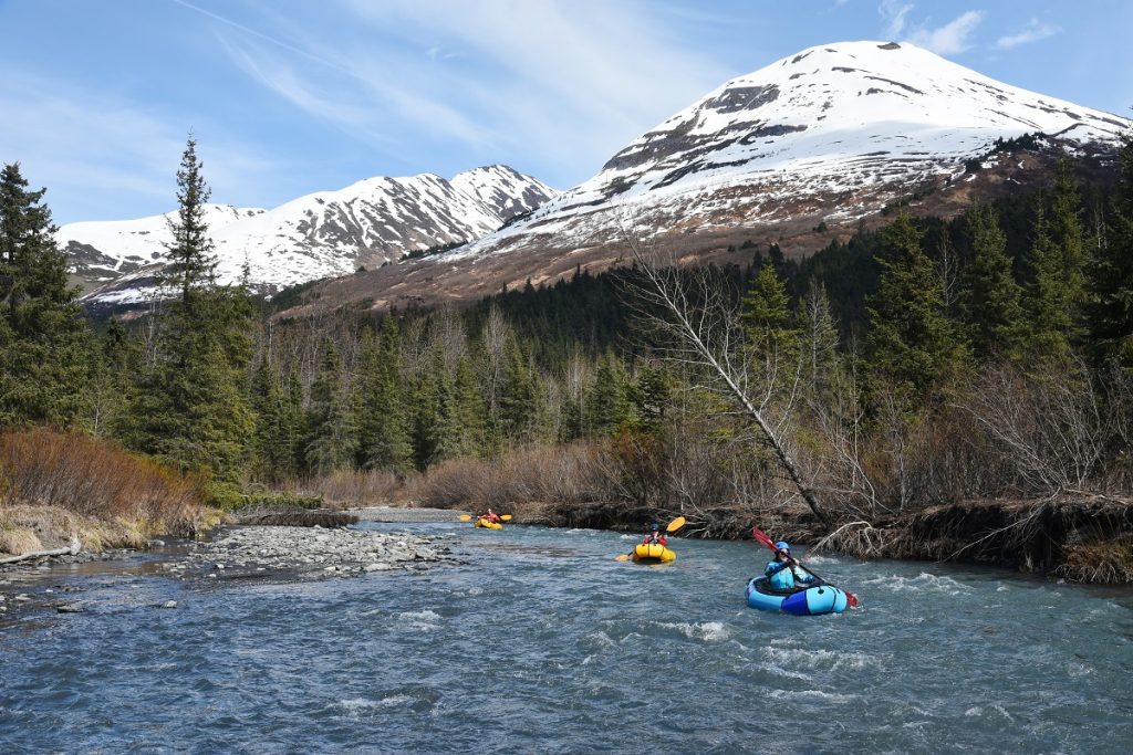 people packrafting on the river with snowy mountain peak in the back