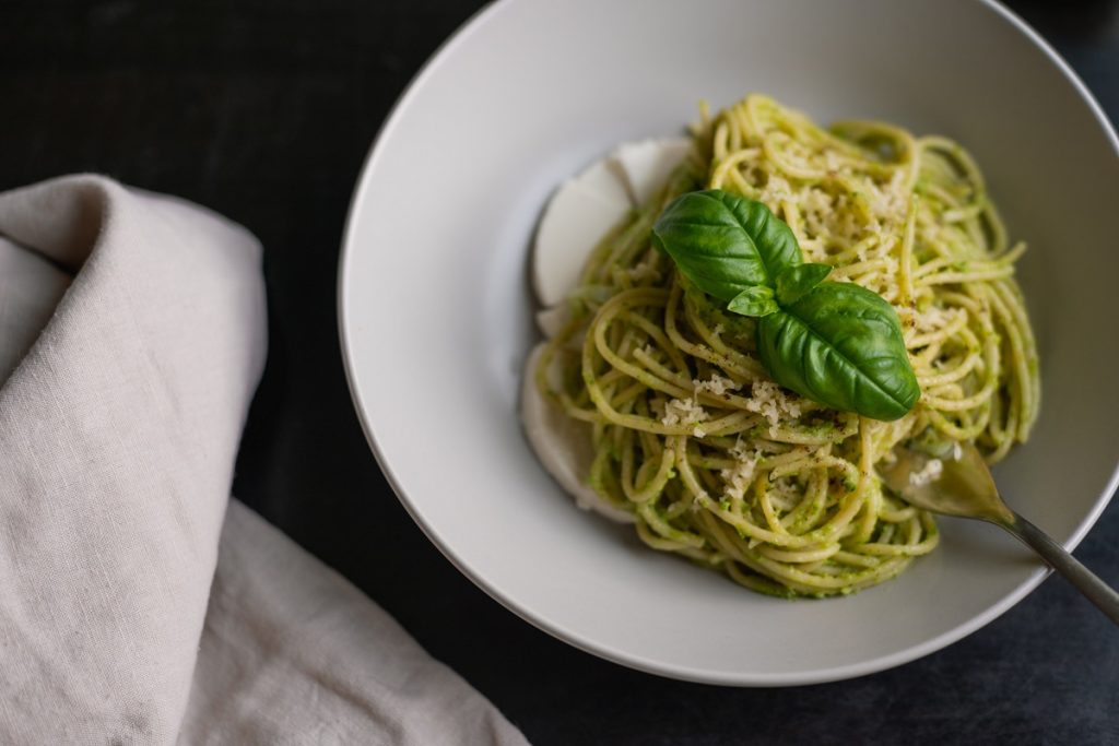 spaghetti with green pesto and basil leaves on top