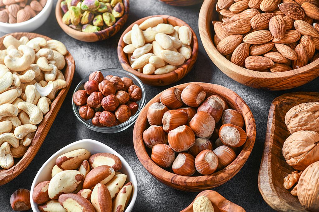Mixed nuts in wooden bowls on black stone table.