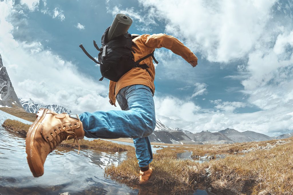 Man hiker jumps across water in mountain area