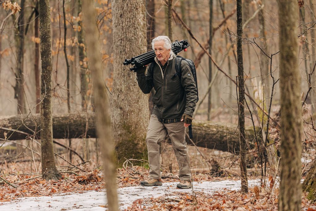 Man carrying photography equipment throug the woods