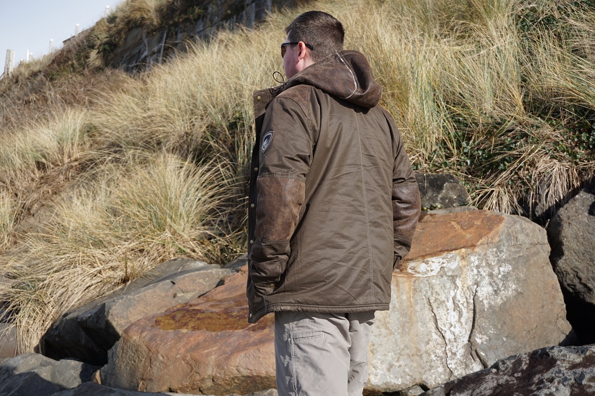 A man standing at a grassy shore on a winter day, wearing KUHL winter hiking jacket.