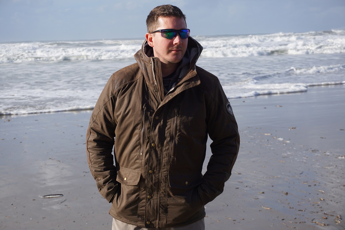 A man with sunglasses standing at a shore on a winter day, wearing KUHL winter hiking jacket.