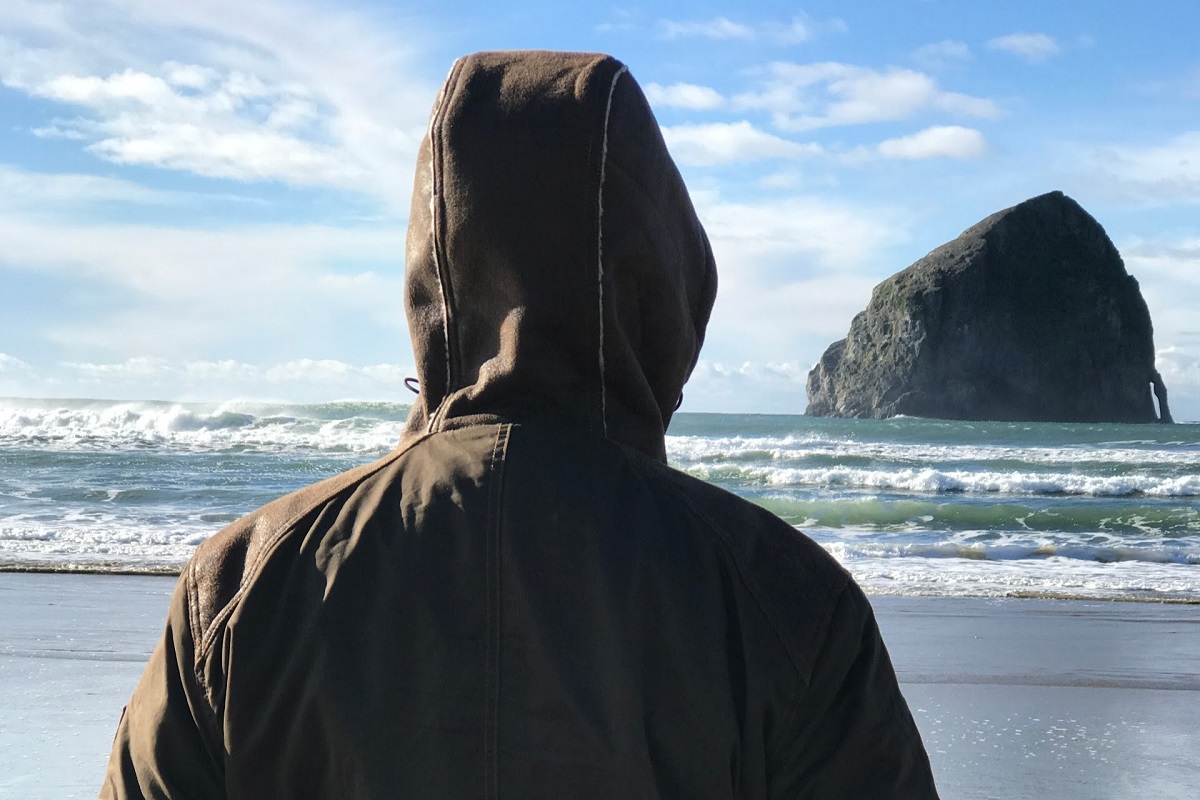 A man standing at a shore on a winter day, wearing KUHL winter hiking jacket with hood up.